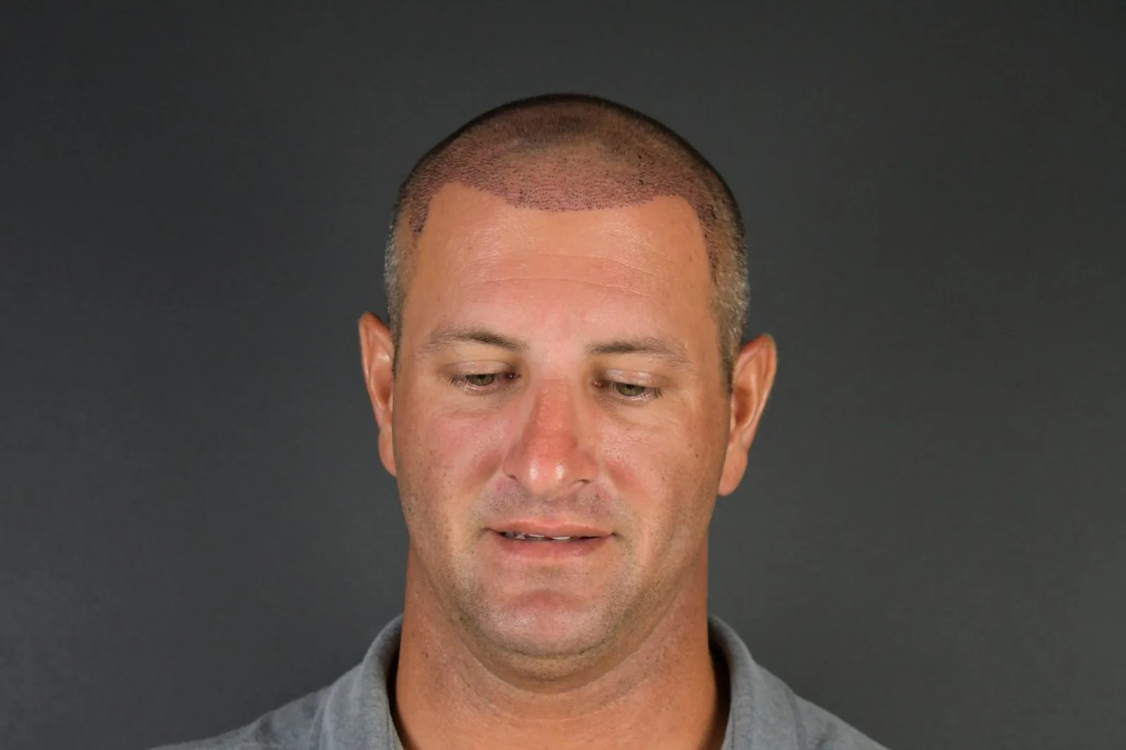 Headshot of a man with short hair wearing a gray shirt against a dark background